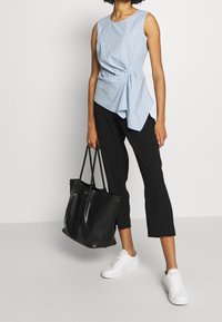 Ljusblå och vit randig ärmlös topp med detalj av sidoknut, ihop med svarta capribyxor och vita sneakers. Svart axelväska ingår.