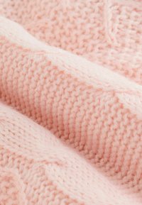 Weicher, rosa gestrickter Stoff mit einem strukturierten Muster, das unterschiedliche Maschendetails aufweist und eine leicht flauschige Textur für zusätzliche Wärme bietet.