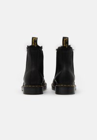 Botas de tobillo de cuero negro con borde de piel sintética negra, lengüetas amarillas y costuras amarillas en la suela. Diseño de suela de goma sólida.
