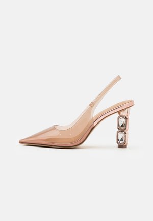 Przezroczysty różowy sandał na obcasie z szpiczastym noskiem i paskiem zapinanym z tyłu; posiada obcas typu blok ozdobiony dwoma kwadratowymi kryształkami.