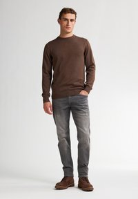 Suéter de punto marrón, jeans grises y botas de tobillo marrones. El suéter tiene un cuello redondo y mangas ajustadas; los jeans son de corte slim con una textura descolorida.