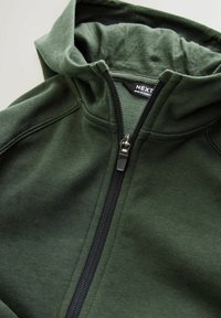 Mørkegrøn zip-up hoodie med en blød tekstur, der har en sort lynlås og hætte. Inkluderer mærkeetiket indeni kraven til identifikation.