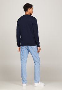 Navyblauwe trui met lange mouwen en een ronde hals, gecombineerd met lichtblauwe spijkerbroeken en witte sneakers, getoond vanaf de achterkant.