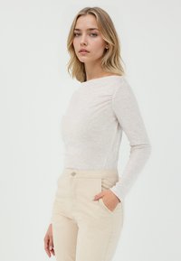 Lichtbeige langemouwen shirt met een ronde hals en een aansluitende pasvorm, gecombineerd met lichtbeige broek met zijzakken.