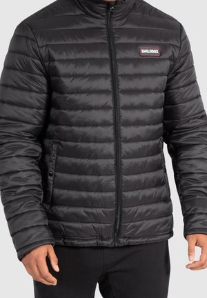 Black puffer jacket with a high collar, horizontal quilted texture, and a front zipper. Features a small red brand patch on the left chest.