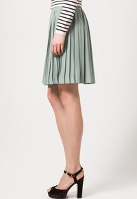 Falda plisada verde menta con cintura elástica, combinada con una camiseta de manga larga a rayas y sandalias negras de tacón alto.