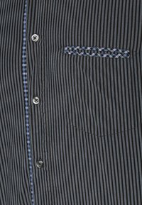 Zwart-grijs gestreept shirt met verticale strepen en subtiele textuur, met een blauw geruite rand bij de borstzak en ronde zwarte knopen.