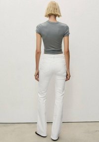 Camiseta ajustada gris, de mangas cortas, combinada con vaqueros acampanados blancos. Textura suave, costuras mínimas y diseño estándar de cinco bolsillos.
