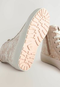 Buty sportowe za sznurowaniu z wzorzystą, jasnoróżową cholewką, białą gumową podeszwą oraz teksturowaną różową podeszwą z motywem kwiatowym.
