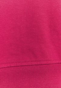 Primer plano de una tela rosa brillante que muestra una costura que divide el material de punto suave de la textura de punto acanalado en el borde inferior.