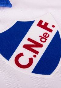 Witte sporttrui met een schildvormig logo in blauw en rood. Het logo bevat de tekst "C.N. de F." in vetgedrukte rode letters.