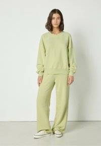 Svetlo zeleni, teksturiran oversized pulover z dolgimi rokavi in usklajenimi širokimi hlačami, v kombinaciji z belimi supergami. Preprost dizajn.