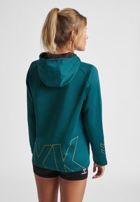 Türkisfarbener Kapuzenpullover mit einem schwarzen Innenfutter. Verfügt über ein orangefarbenes Logo auf der Rückseite und lange Ärmel mit einer schlanken Passform.