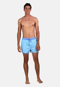 Shorts de bain bleus avec un motif léger, taille élastique avec cordon de serrage et poches latérales, fabriqués en matériau à séchage rapide. Modèle debout pieds nus.