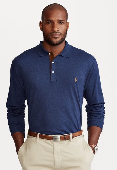 Navy langärmig poloshirt met een bruine kraag, twee knopen en een geborduurd logo. Gecombineerd met beige broeken en een bruine riem.