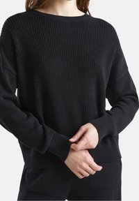 Czarny sweter z dzianiny z teksturowanym wzorem, szerokim dekoltem i długimi rękawami. Posiada ściągacze przy mankietach i u dołu, co nadaje mu dopasowany kształt.