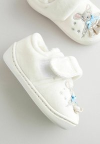 Chaussons en peluche blancs pour tout-petits avec une sangle Velcro, présentant un design de lapin avec des accents bleus et des broderies d'étoiles argentées sur le côté.