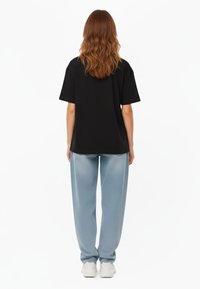 T-shirt nera oversize a maniche corte, abbinata a pantaloni larghi blu chiaro. L'outfit è completato da sneakers bianche.