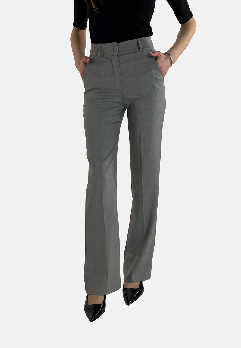Pantalon tailleur gris avec une taille haute, un devant plat et des poches latérales. Le tissu a une texture subtile, associé à des talons noirs brillants.
