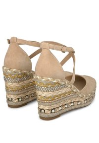 Sandalias de cuña de ante beige con correas cruzadas en el tobillo, acentos decorativos de yute trenzado y cuentas a lo largo de la plataforma. Detalles de superficie texturizada.