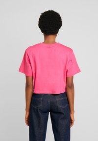 Camiseta corta de manga corta en algodón de color rosa brillante. Cuello redondo simple con una textura suave, combinada con pantalones vaqueros de mezclilla azul oscuro.