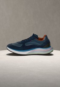 Basket bleu marine avec doublure intérieure orange, semelle blanche comportant des bandes bleues, rouges et vertes, présentée sur une surface claire avec un fond gris.