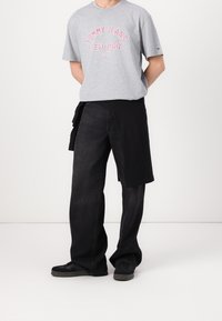 Szara bawełniana koszulka z czerwonym napisem "TOMMY JEANS NEW YORK CITY", zestawiona z czarnymi szerokimi spodniami dżinsowymi i czarnymi sportowymi butami.