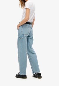 Jeans sueltos de color azul claro con cintura alta, cinco bolsillos y costuras visibles, combinados con una camiseta blanca ajustada y zapatos negros.