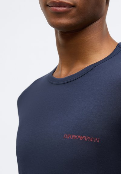 Sötétkék pamut póló kerek nyakkivágással és piros "Emporio Armani" logóval a mell bal oldalán. Sima tapintású.
