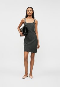 Vestido de denim gris con escote cuadrado y tirantes finos. La modelo sostiene un clutch negro y lleva unas bailarinas beige. Diseño simple y ajustado.