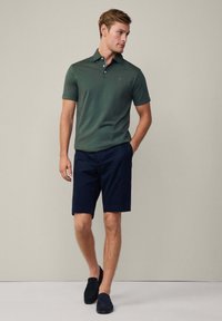 Tmavě zelené polokošile s krátkým rukávem a dvouknoflíkovým zapínáním, v kombinaci s námořnickými kraťasy. Model má na sobě námořnické slip-on boty.