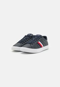 Sneaker in pelle blu navy con suola in gomma bianca, dotate di una tomaia testurizzata, punta rotonda e accenti rossi e bianchi sui lati.
