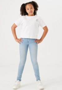 Weißes, kurzärmliges Baumwoll-T-Shirt mit einem grafischen Design auf der Brust; kombiniert mit hellblauen, engen Jeans und weißen Turnschuhen.