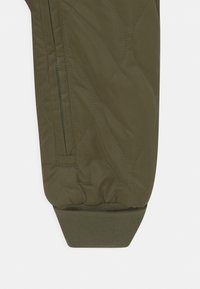 Zielona oliwkowa pikowana kurtka, z zamkiem błyskawicznym w kieszeni i ściśniętymi mankietami, zaprojektowana w wąskiej sylwetce.