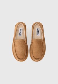 Brune ruskind slip-on sko med et blødt indvendigt foer, der har et syet sko-design og flad gummisål. Mærket er synligt indeni.