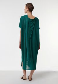 Vestido verde, ligero, de longitud hasta la rodilla con espalda drapeada, mangas cortas y aberturas laterales. Hecho de tela transparente, presenta un ajuste holgado.