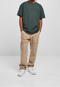 Tmavě zelené tričko s krátkým rukávem, volný střih; béžové cargo kalhoty s bočními kapsami; bílé tenisky s texturovaným povrchem.