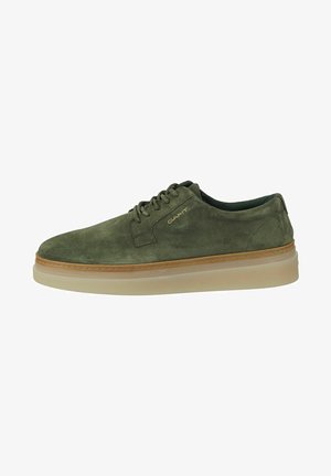 Chaussure en daim vert à bout arrondi, avec un design à lacets et une semelle légère et amortie. Présente un logo discret sur le côté et un bord contrastant couleur tan.