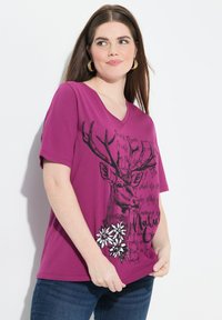 T-shirt à col en V et manches courtes en fuchsia, ornée d'un graphique noir représentant un cerf avec des bois et des accents floraux blancs en bas à droite.