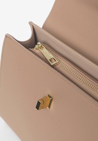 Borsa in pelle beige chiaro con finitura testurizzata, chiusura con cerniera dorata e un accento metallico geometrico sul davanti.