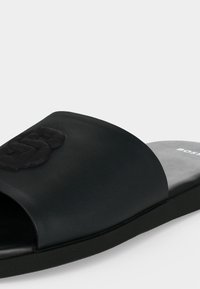 Sandale slide noire à bout ouvert avec logo en relief sur la bride et semelle intérieure moulée avec le nom de la marque.