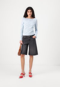 Light blue lace long-sleeve top with floral pattern, paired with dark gray denim bermuda shorts and red high-heeled shoes. Brown bag in hand.