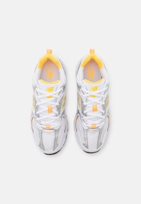 Baskets de course blanches en mesh avec des accents argentés, des touches orange et une semelle texturée. Comprend un col rembourré et un système de laçage.