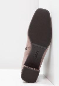 Brązowy zamszowy but z teksturowaną gumową podeszwą. Charakteryzuje się lekko zakrzywionym obcasem oraz markową wkładką. Wyprodukowano w Portugalii.