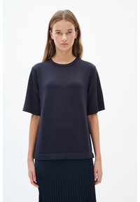 Ciemnoniebieska koszulka z krótkim rękawem z miękkiego materiału, z okrągłym dekoltem, charakteryzująca się luźnym krojem i lekko opadającym dołem po bokach.