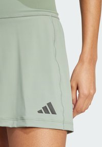 Falda deportiva verde claro con una textura suave, detalles de costura y un logo negro de Adidas con tres rayas diagonales en el dobladillo.