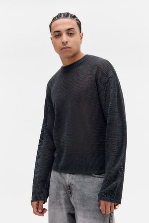 Pull en maille noire à manches longues avec un design en tricot texturé, doté d'un col rond et de manches tombantes, associé à un jean gris délavé.
