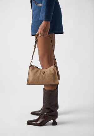 Borsa a tracolla in pelle beige con motivi in rilievo, forma curva nella parte superiore e tracolla regolabile; indossata con stivali in pelle marrone al ginocchio.