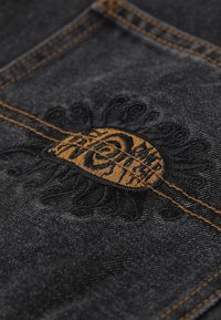 Black denim fabric featuring intricate golden embroidery with a circular design. Contrast stitching in orange highlights the seams.