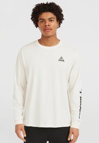 T-shirt bianco a maniche lunghe in cotone, con un logo triangolare sul lato sinistro del petto e testo in grassetto lungo la manica destra.